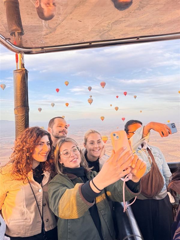 Amici che si scattano un selfie nella cesta di un volo condiviso con le mongolfiere sullo sfondo